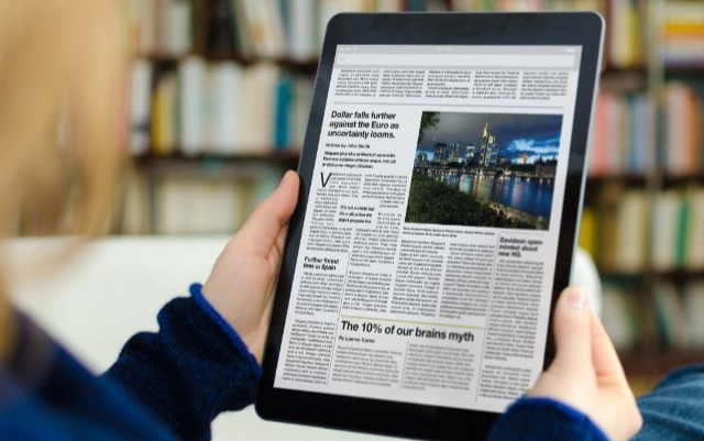 Hands holding tablet with news article displayed. 