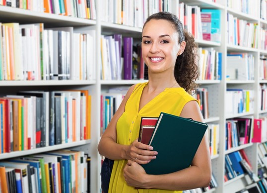 Girl holding books in front of bookshelves